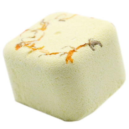 A pale cream-colored square shower steamer tablet topped with real dried green botanical herbs.