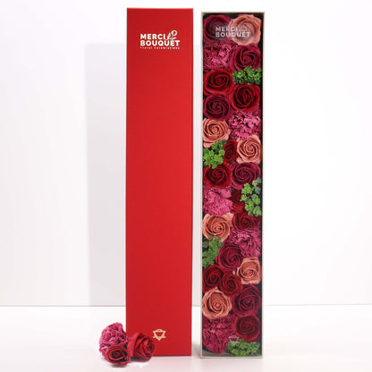 A tall, slim red gift box showcasing classic floral illustrations and filled with luxury rose-themed bath treats.
