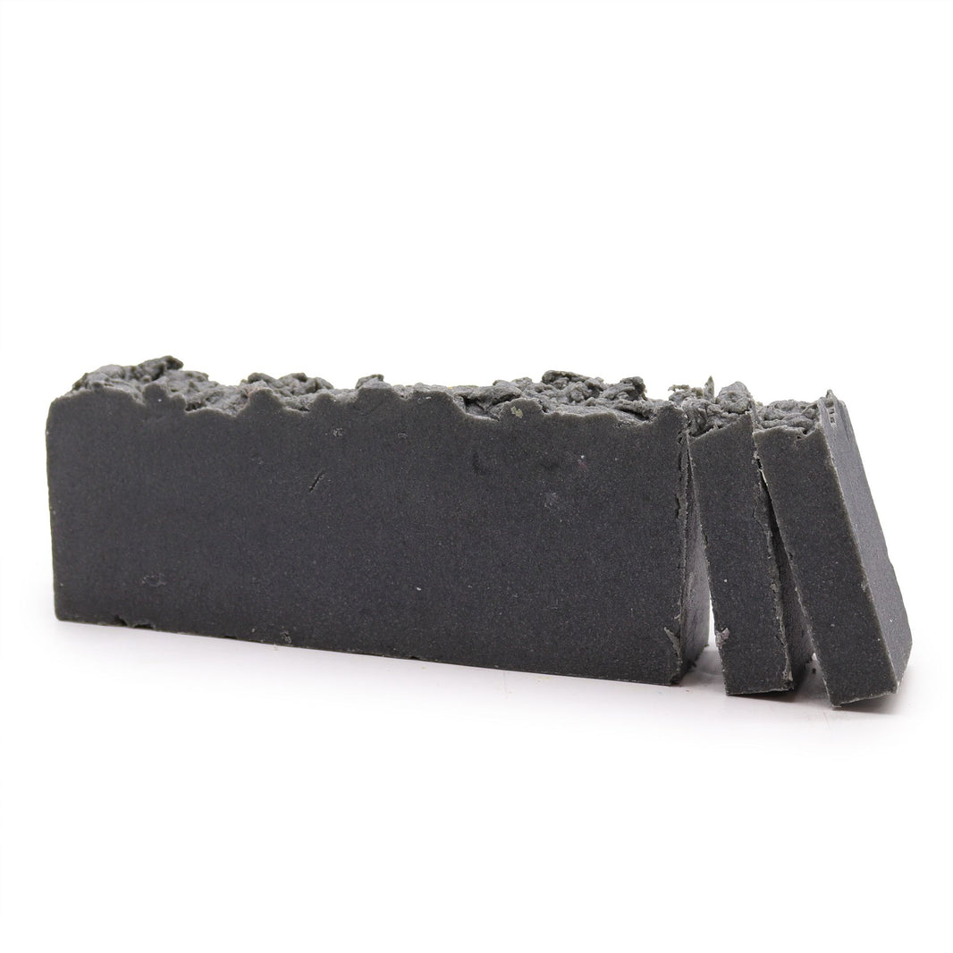 A rectangular artisan soap slice with a dark, charcoal-toned textured surface and visible natural exfoliating grains.