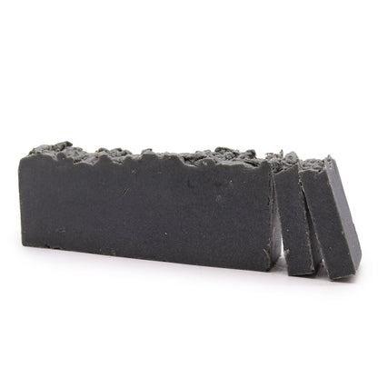 A rectangular artisan soap slice with a dark, charcoal-toned textured surface and visible natural exfoliating grains.