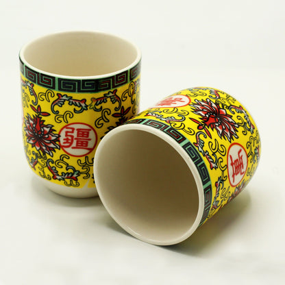 Two ceramic tea cups featuring a vibrant yellow and green oriental pattern with traditional floral motifs.