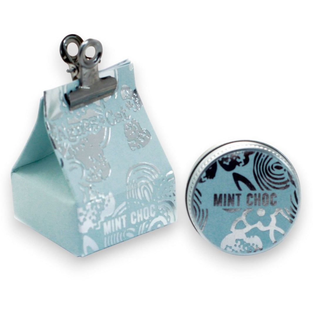 A 20g round tin of mint chocolate scented lip balm shown with its teal and brown festive dessert-themed gift box.