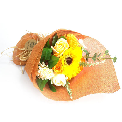 A standing bouquet of bright orange soap flowers wrapped in decorative orange and yellow paper with a ribbon.