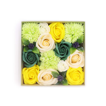 A square gift box filled with realistic yellow and green soap flowers, looking like a fresh Spring garden arrangement.