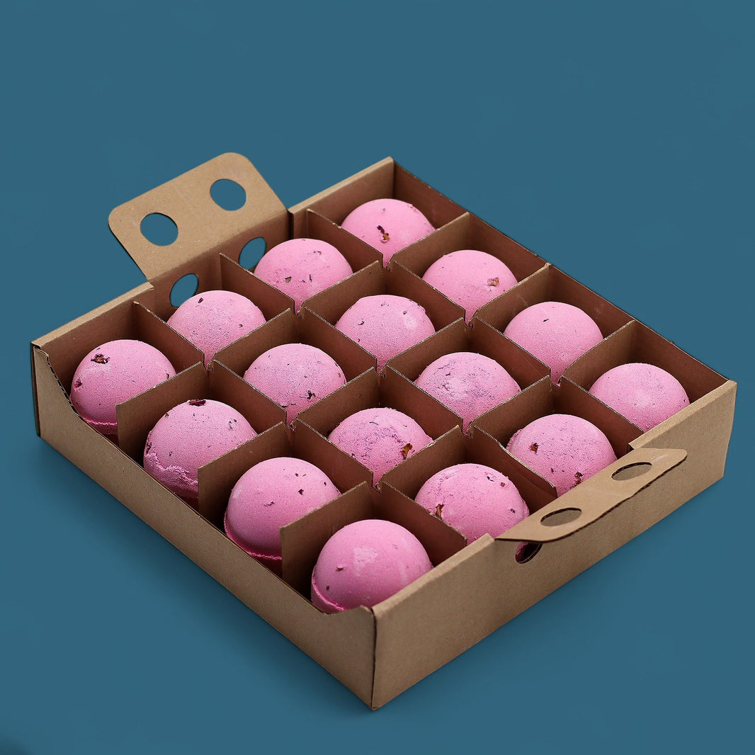 A cardboard display box containing 16 individually wrapped 180g pink bath bombs decorated with real dried flower petals.