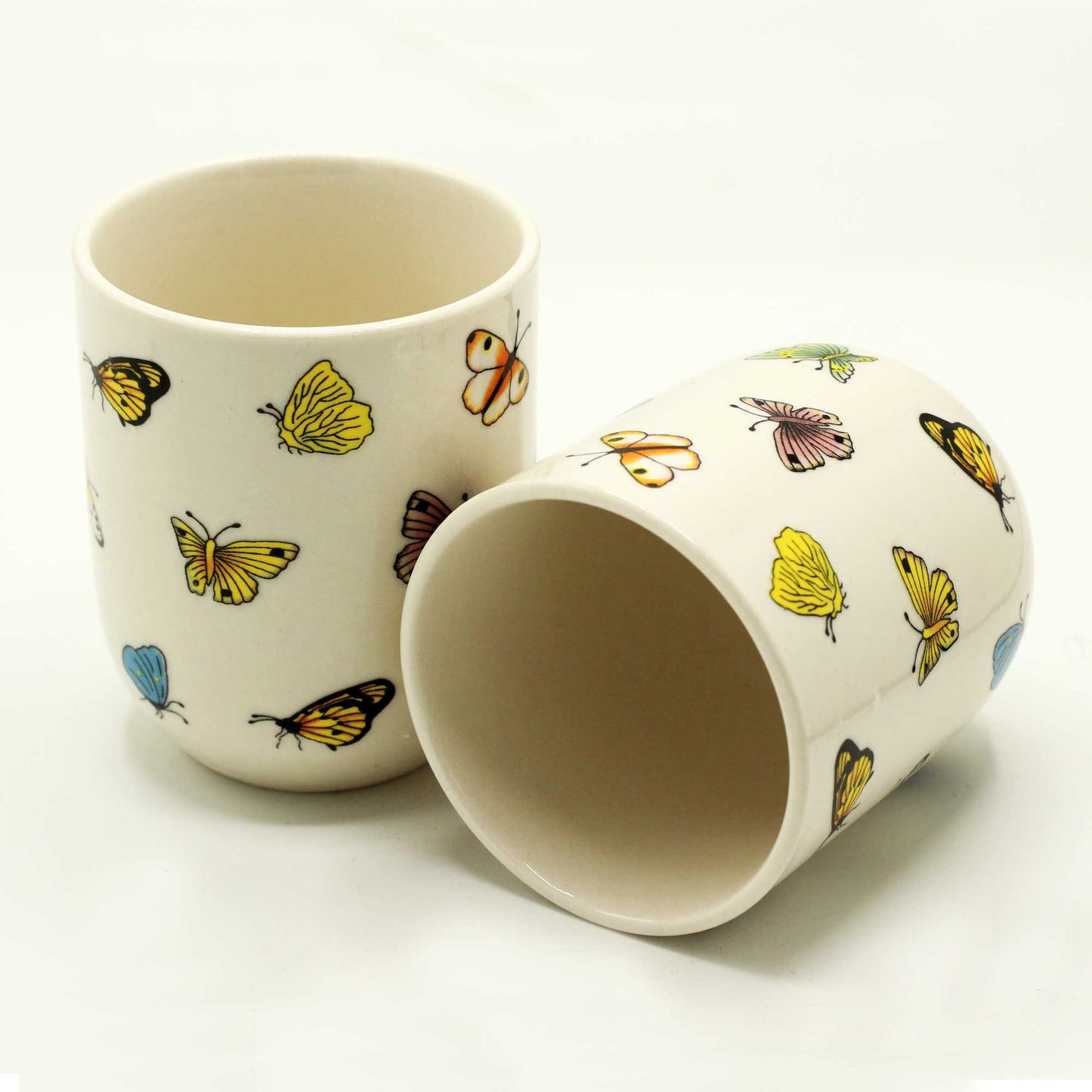 A set of two ceramic tea cups decorated with colorful butterfly and wildflower patterns.