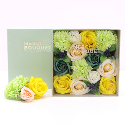 A square gift box filled with realistic yellow and green soap flowers, looking like a fresh Spring garden arrangement.