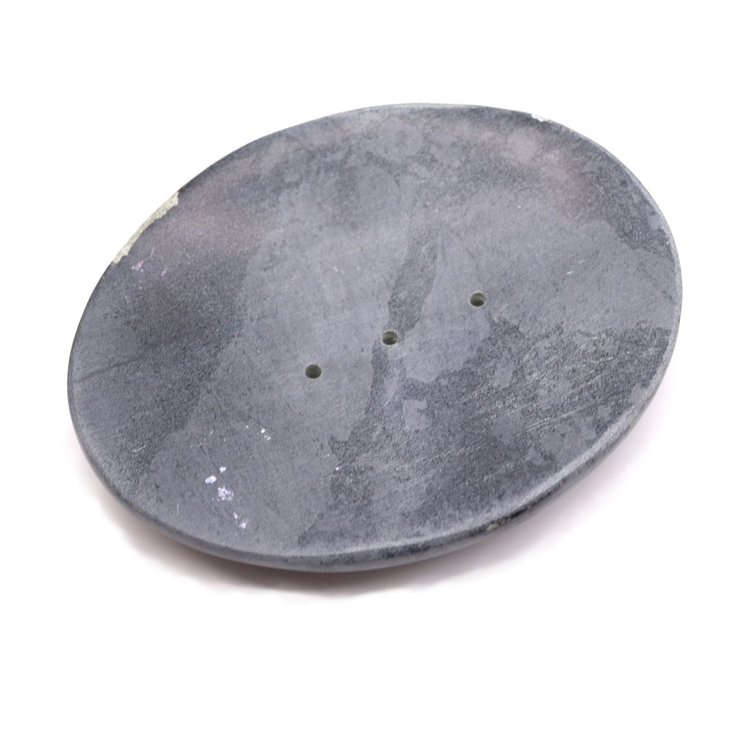 A heavy, oval-shaped soap dish carved from natural grey soapstone with organic textures and drainage slats.