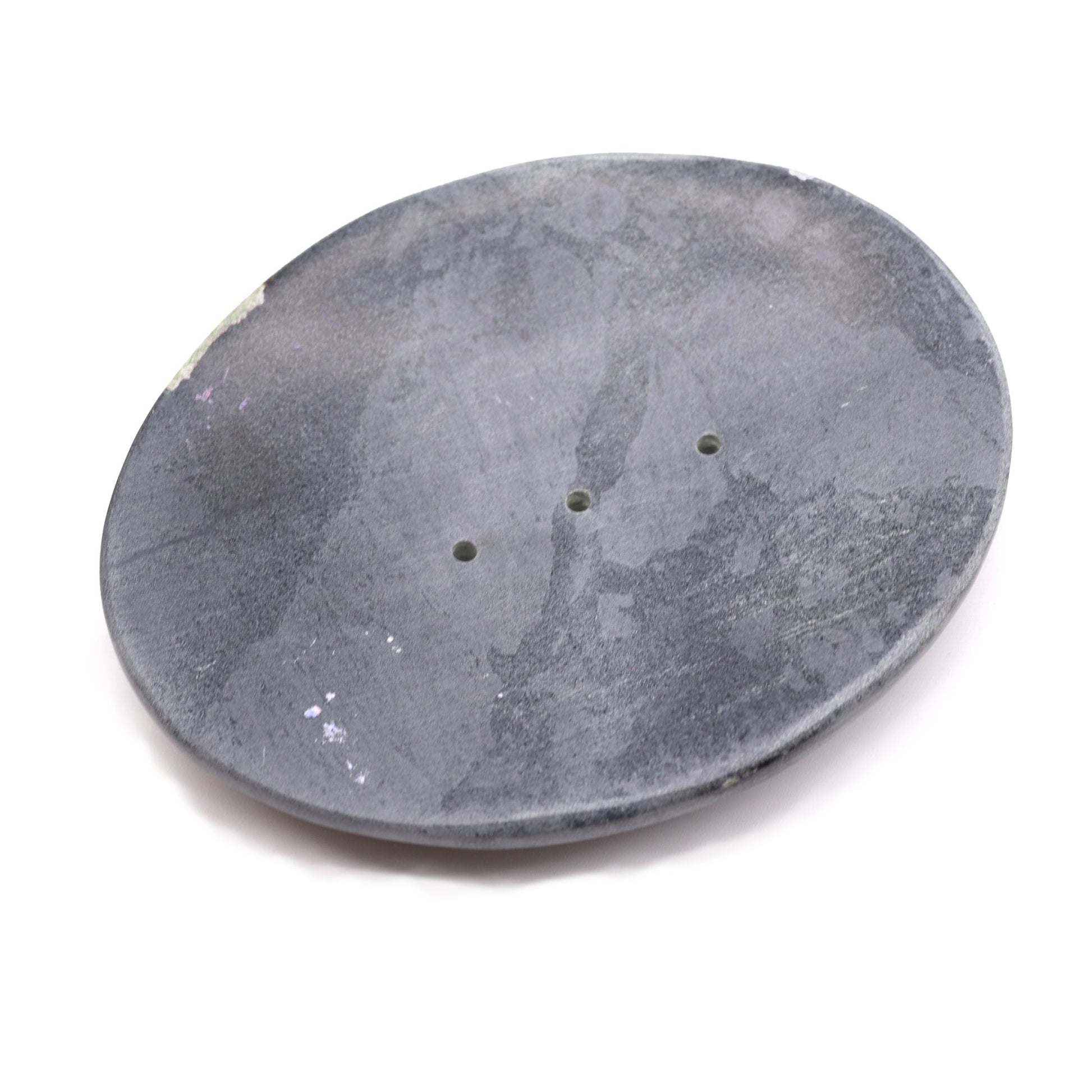 A heavy, oval-shaped soap dish carved from natural grey soapstone with organic textures and drainage slats.