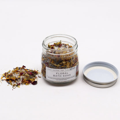 A clear glass jar filled with a premium blend of white bath salts and vibrant, multi-colored dried flower petals.