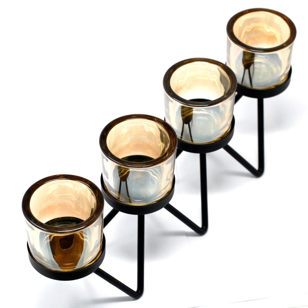 A modern black iron candle holder featuring a zigzagging metal frame that supports four separate clear glass votive cups.