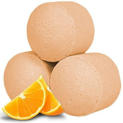 A large bulk collection of small, orange-colored bath bomb "pills" shown with fresh orange slices for a vibrant presentation.