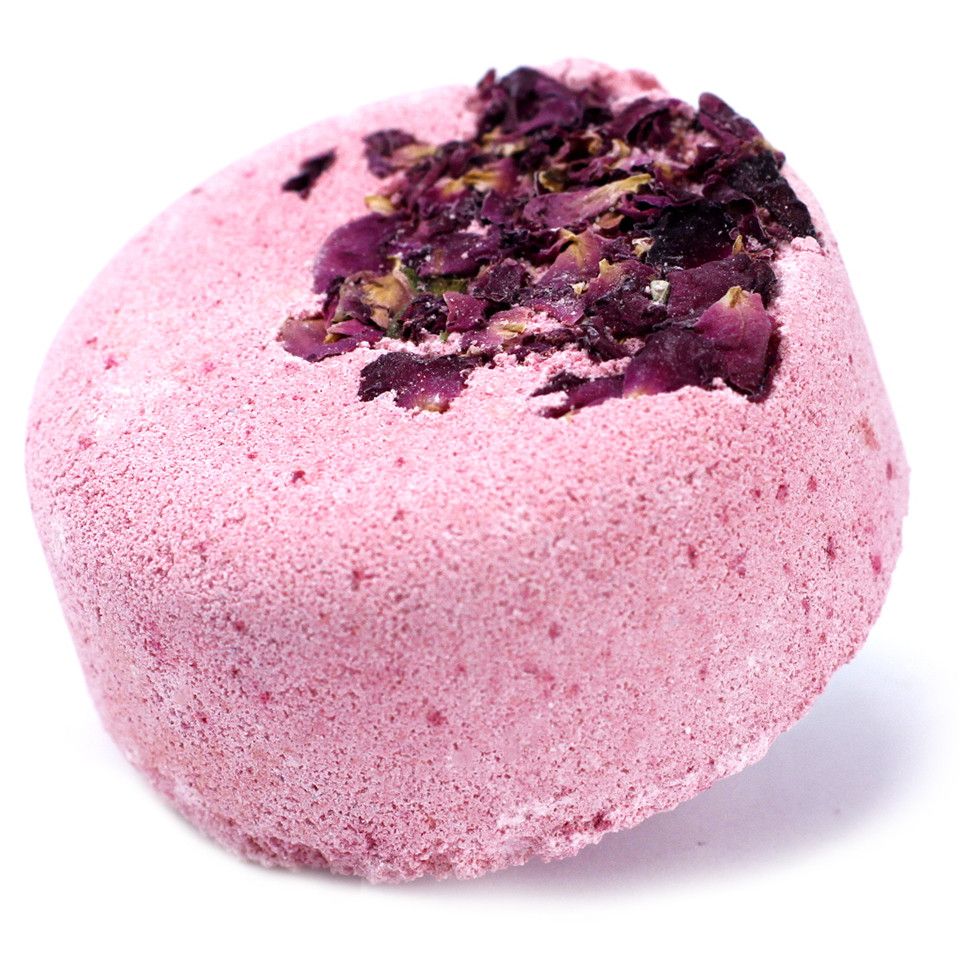 A soft pink bath bomb generously topped with a layer of dried red rose petals for a premium bath experience.