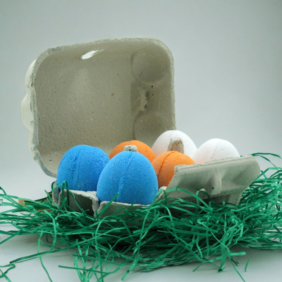 A pack of 6 vibrant, egg-shaped bath bombs in an egg tray, featuring different bright colors for a fun and fragrant bath.
