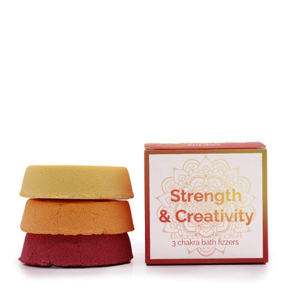 A small white gift box containing two square bath fizzers in vibrant red and orange, labeled for Strength and Creativity.