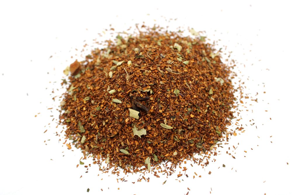 A high-volume pile of red rooibos tea leaves blended with digestive-friendly herbs and seeds.