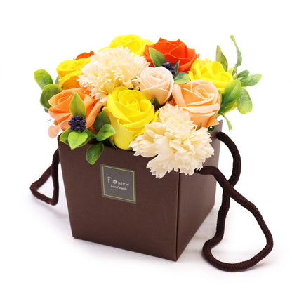 A vibrant arrangement of yellow, orange, and white soap flowers in a gift box, looking like a real Spring floral bouquet.
