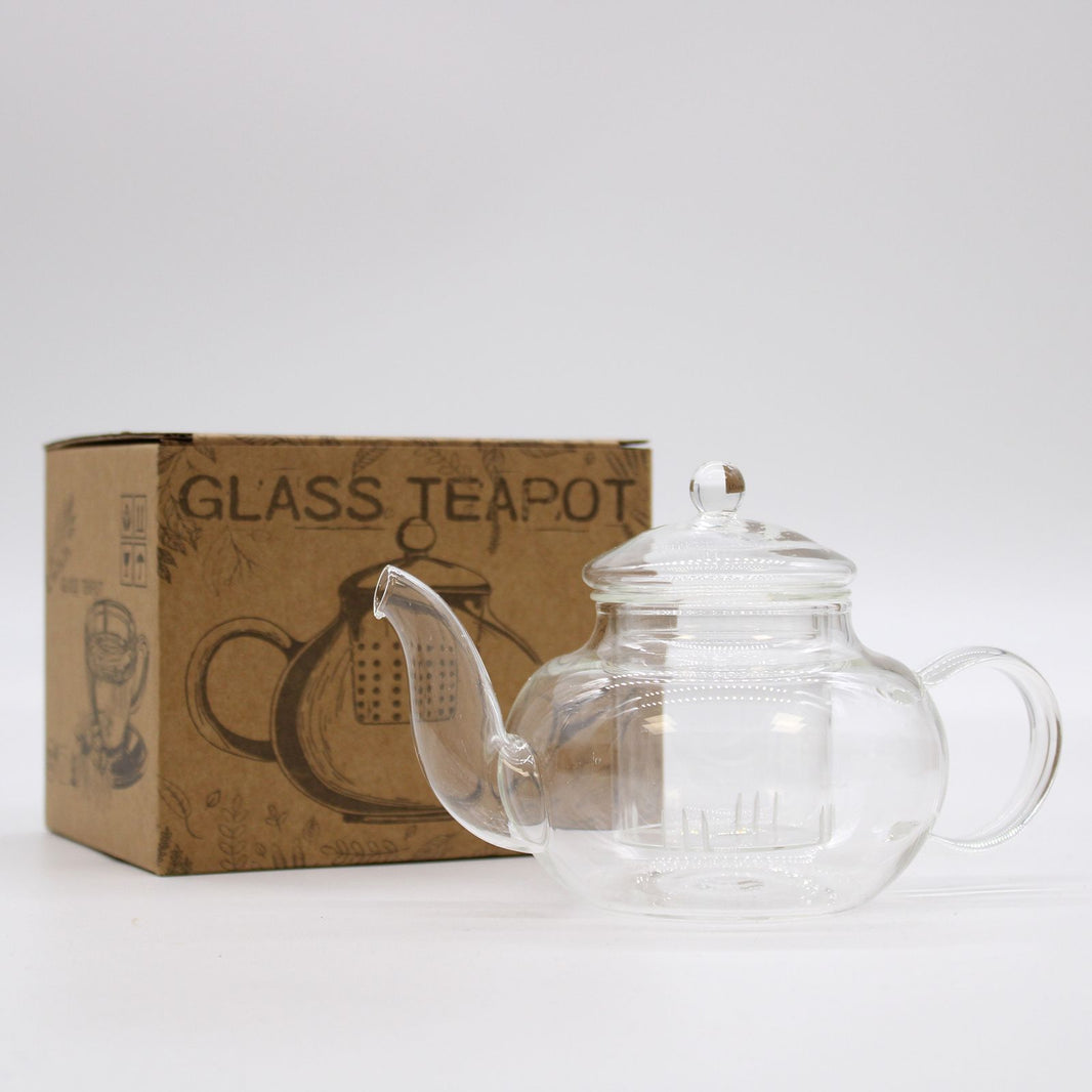 A small, clear glass teapot designed for individual use, packaged in a rustic kraft cardboard box.