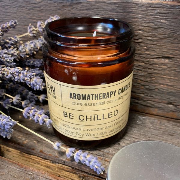A dark amber glass apothecary jar filled with soy wax and a minimalist beige label with bold black "Be Chilled" text.