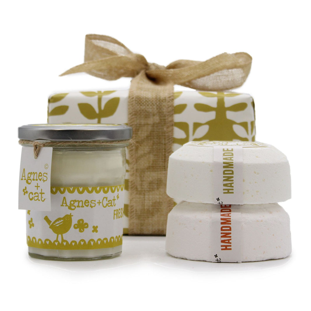 A luxury spa gift box containing a citrus-scented candle and large artisan bath fizzers, tied with a cream-colored bow.