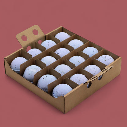 A cardboard display box holding 16 individually wrapped 180g lavender and seed bath bombs in soft blue-grey tones.
