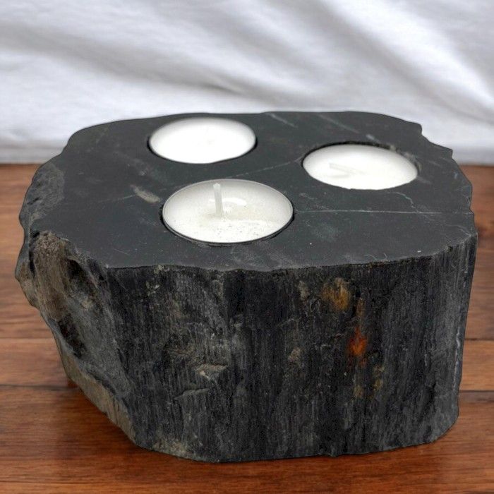 A large, rustic triple candle holder made from a solid piece of natural petrified wood with three slots for tealight candles.