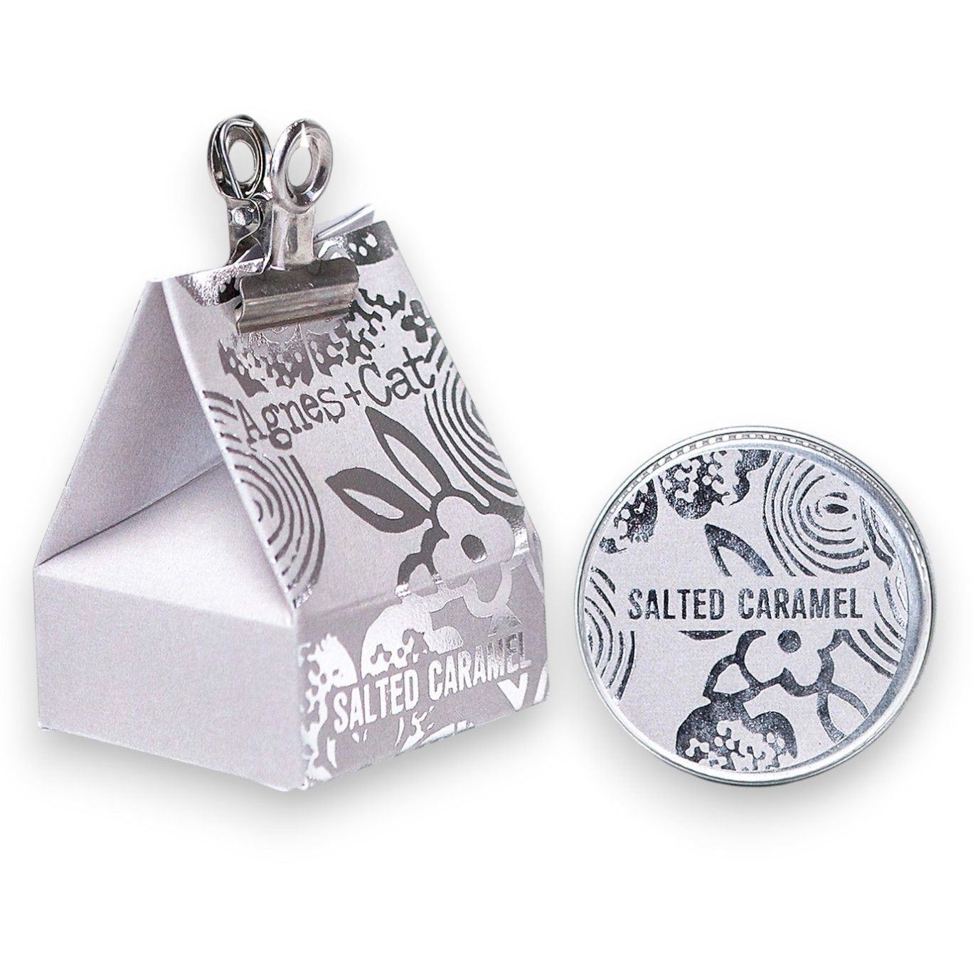 A 20g round tin of salted caramel lip balm shown with its silver and white gift box packaging.