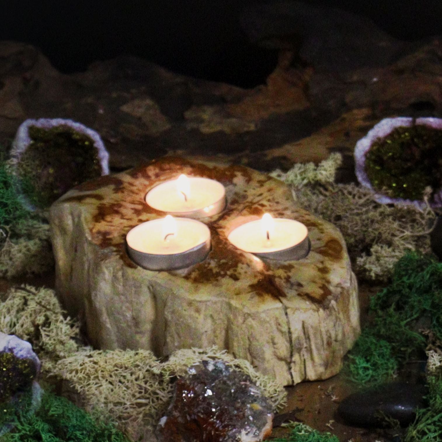 A large, rustic triple candle holder made from a solid piece of natural petrified wood with three slots for tealight candles.