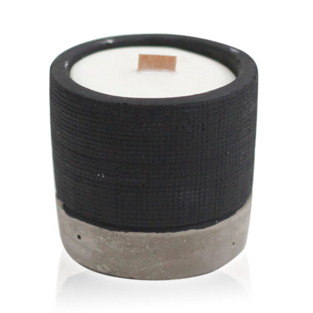 A sleek black concrete candle pot containing a hand-poured soy candle, styled for a modern and moody home interior.